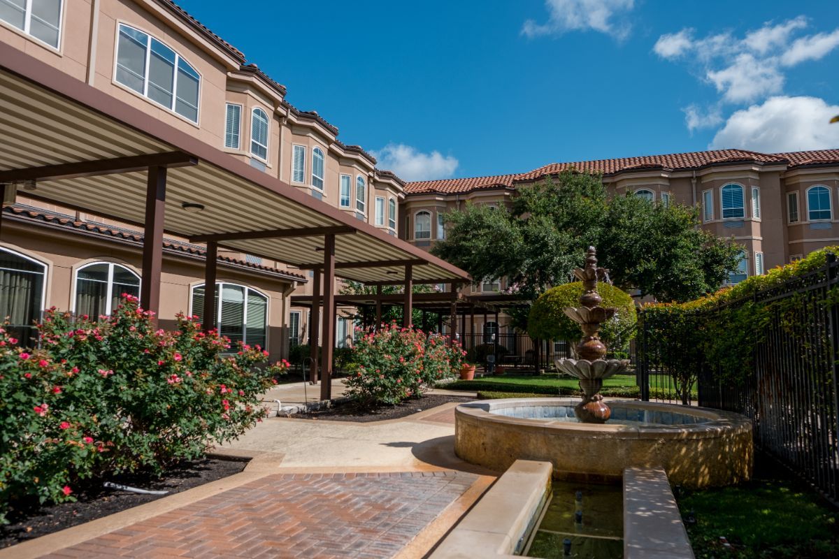 A serene residential courtyard featuring a landscaped garden and a central fountain under a clear blue sky.