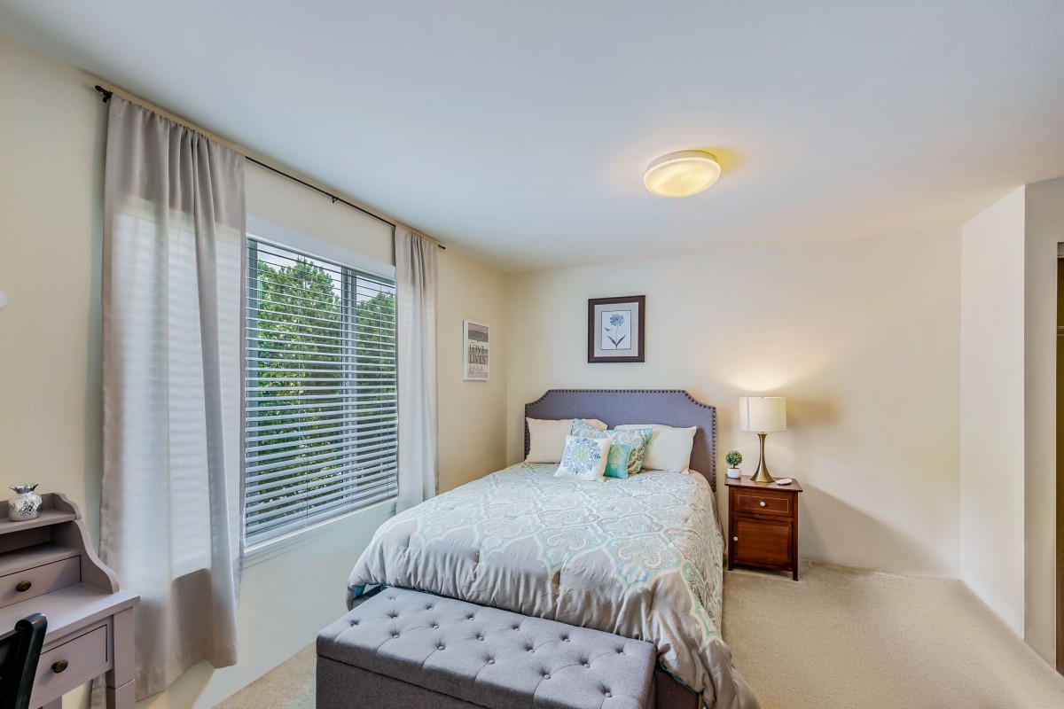 A cozy bedroom with a neatly made bed, a window with curtains, and a lamp on the nightstand.