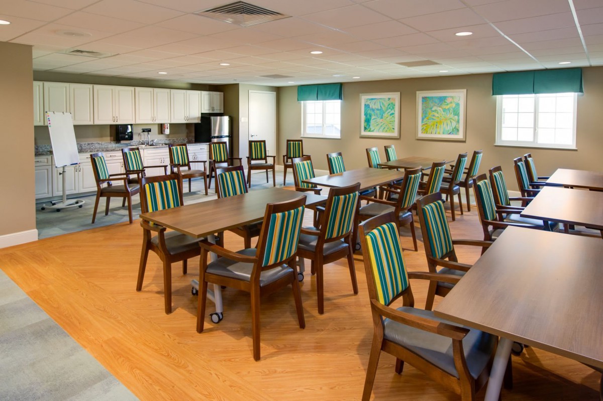 A well-arranged dining area with multiple tables and chairs, adjacent to a kitchen space.