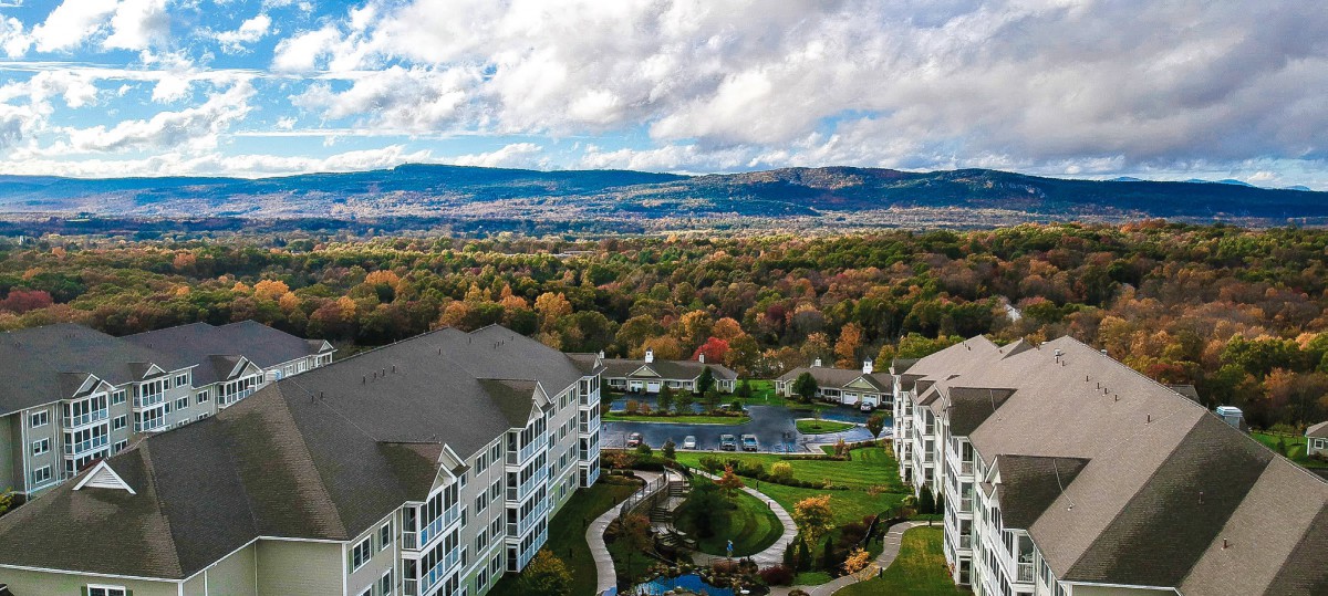 A scenic aerial view of a resort nestled amidst autumnal foliage with mountains in the background.