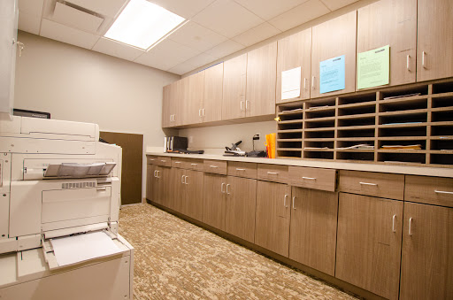 A modern office breakroom featuring cabinets, a printer, and organized mail slots.