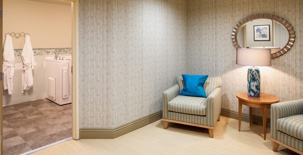 A cozy corner with a striped armchair and a blue cushion against a patterned wallpaper.