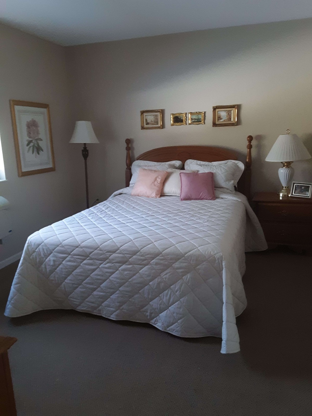 A cozy bedroom with a neatly made bed adorned with a white quilt and pink pillows, flanked by lamps on bedside tables.