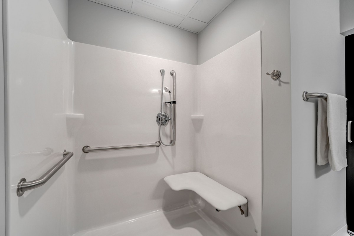Accessible shower with safety features including grab bars and a folding seat.
