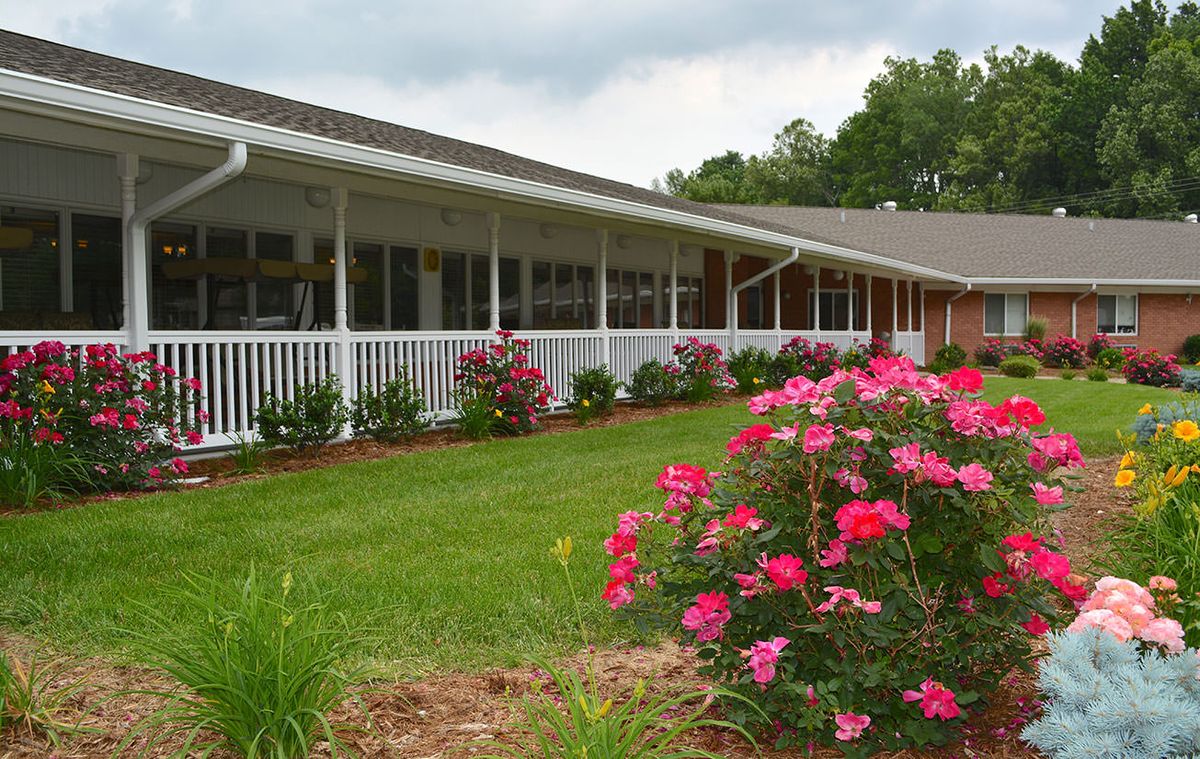 A building with a white porch surrounded by vibrant flowers and greenery.