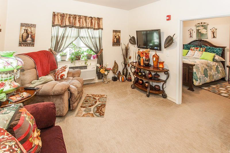 A cozy living room with comfortable seating, a wall-mounted television, decorative accents, and natural light from a window with draped curtains.