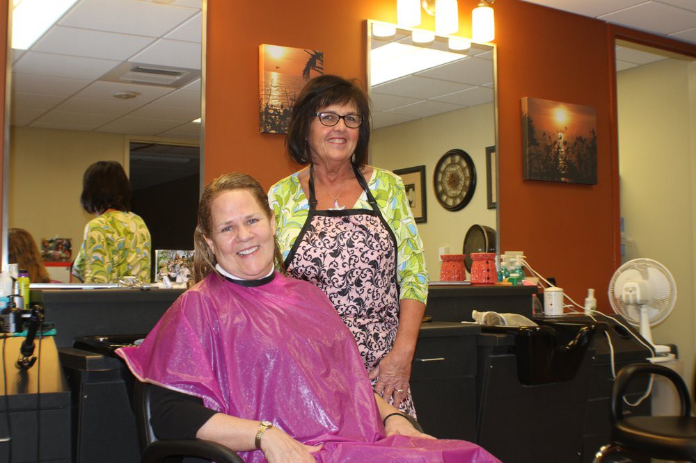 A hairstylist with a client in a hair salon, both smiling for the camera.