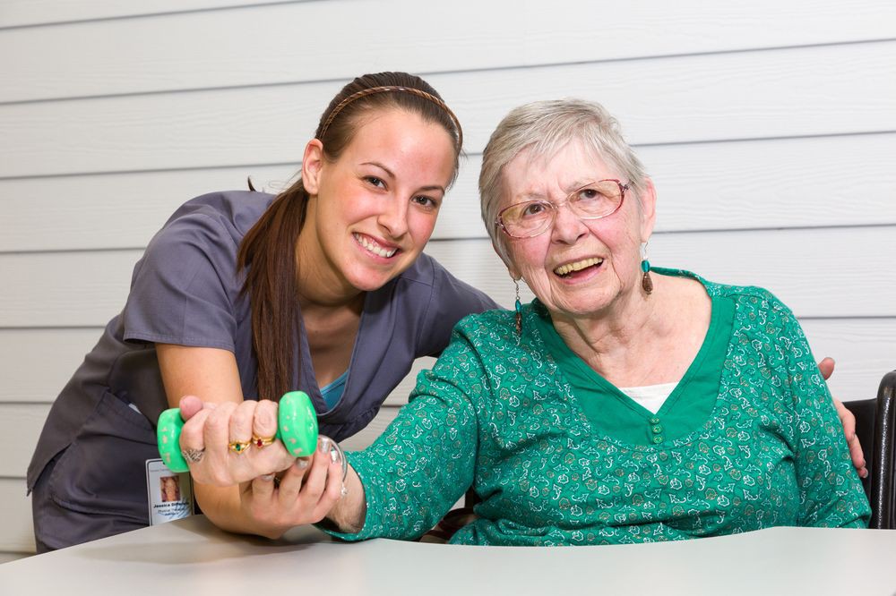 A caregiver assists an elderly woman with physical therapy exercises.