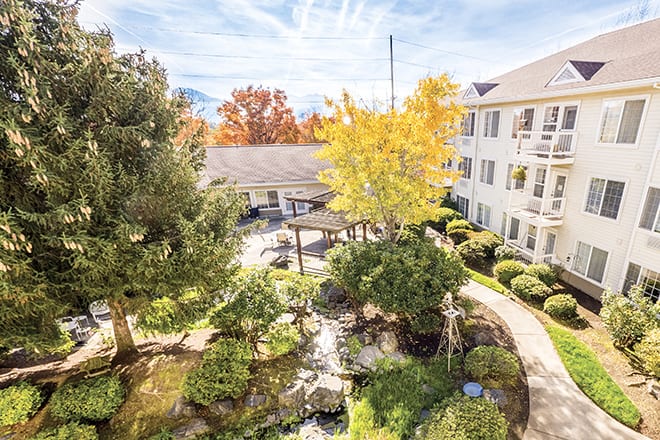 A serene courtyard with lush gardens surrounded by a multi-story building, featuring vibrant autumn foliage.