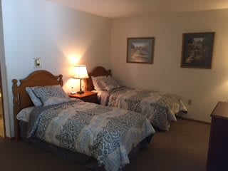 A cozy bedroom with two twin beds, a nightstand with a lamp, and decorative paintings on the wall.