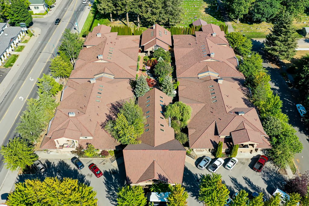 Aerial view of a housing complex with rooftops, surrounded by trees and a driveway with parked cars.