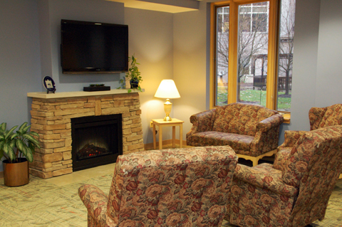 A cozy living room setup featuring comfortable seating, a warm fireplace, and natural light from large windows.