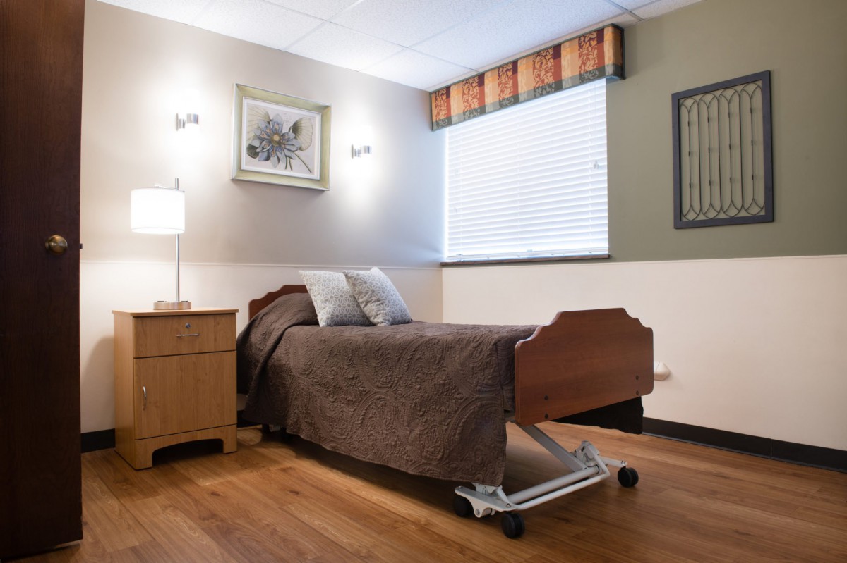 A well-lit hospital room featuring a bed, nightstand, and decorative artwork.