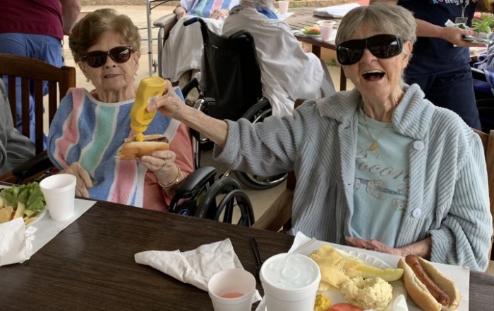 Two elderly women wearing sunglasses enjoy a meal together outdoors.