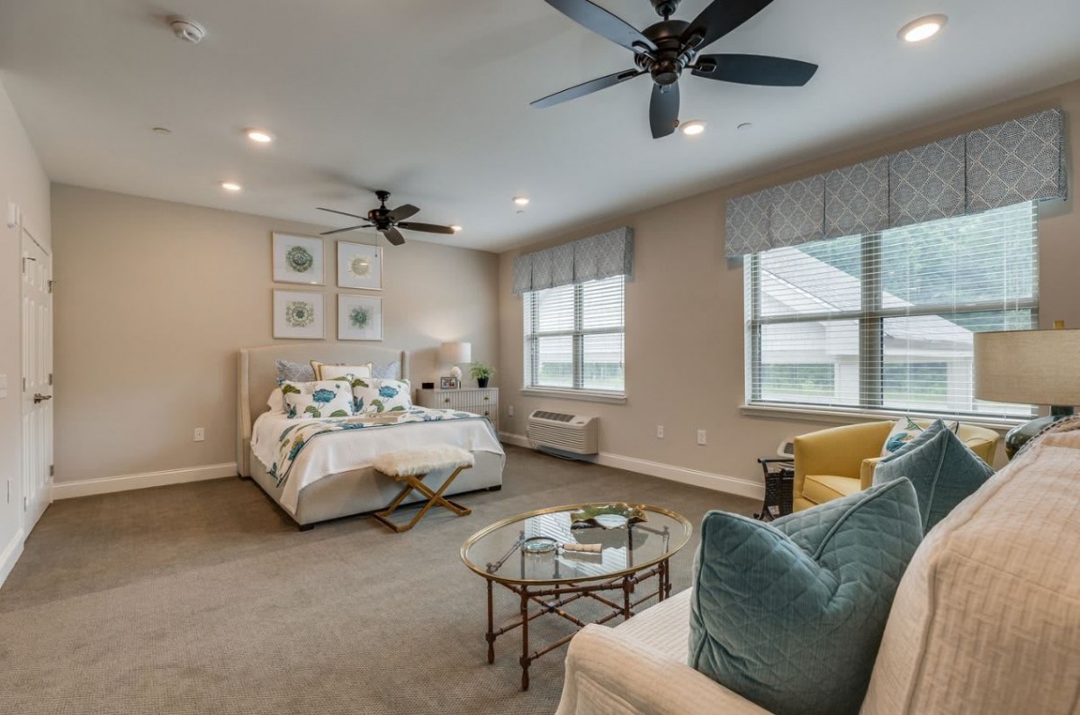 A modern bedroom with neutral tones, featuring a cozy bed, ceiling fans, and stylish furniture.