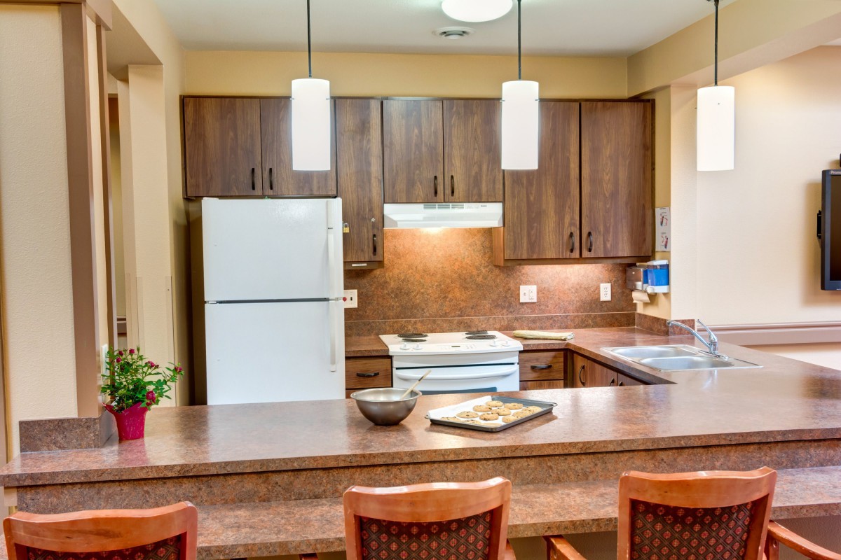 A modern kitchen with wooden cabinets, white refrigerator and stove, featuring pendant lighting and a countertop seating area.