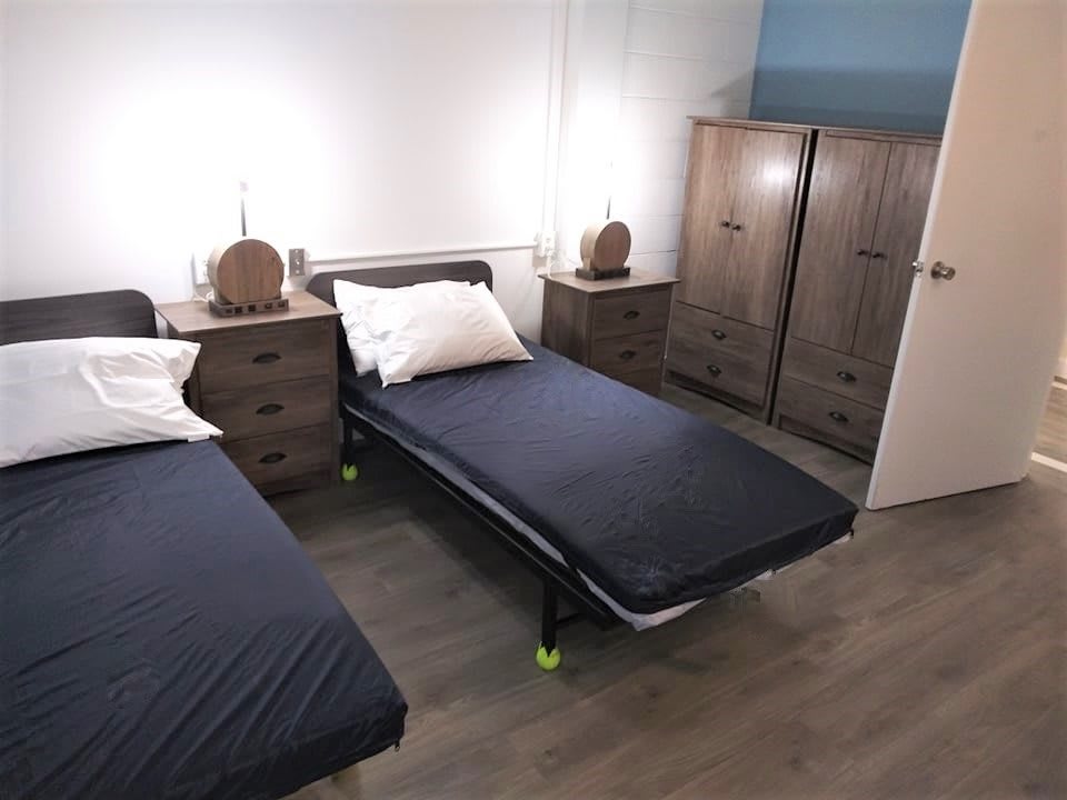 A modern bedroom with two single beds, nightstands, and a wardrobe.