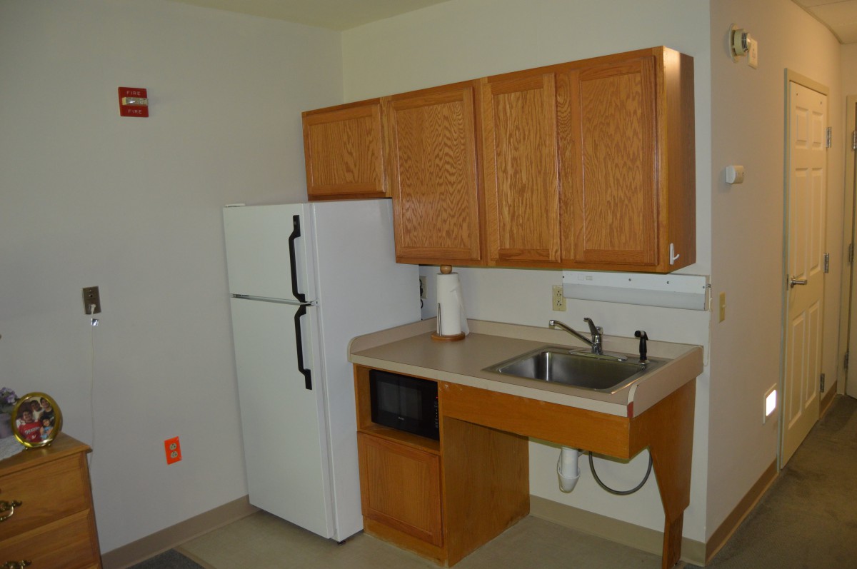Compact kitchen with wooden cabinets, a refrigerator, a microwave, and a sink.