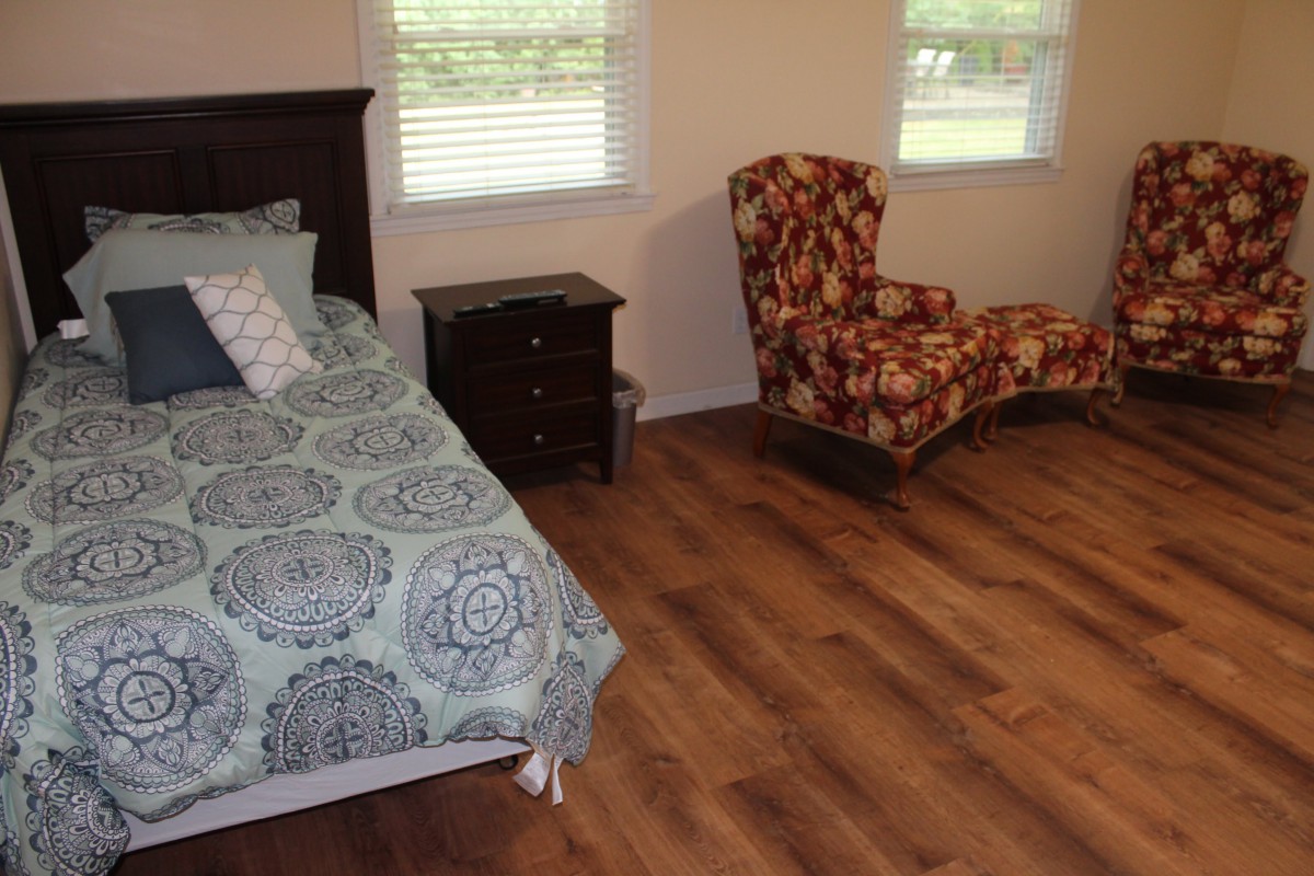 A cozy bedroom with a bed, patterned chair, and wooden flooring.