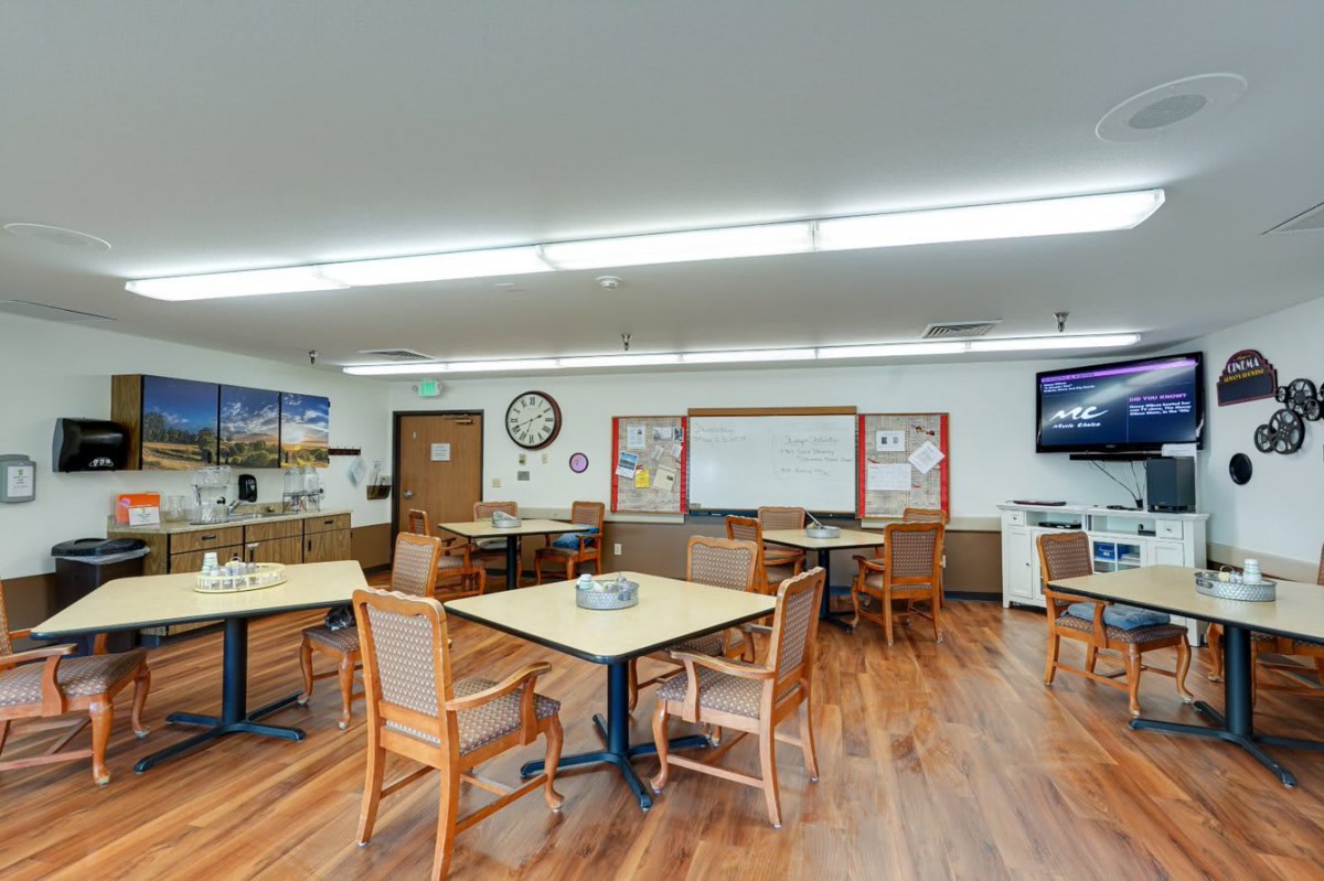 A classroom with tables, chairs, and a whiteboard, featuring a wooden floor and educational posters.