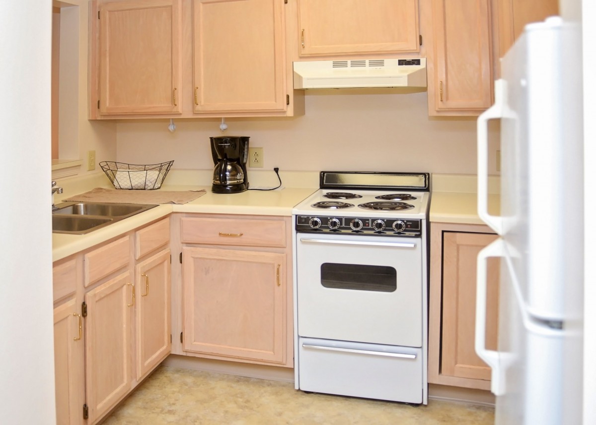 A cozy kitchen with light wooden cabinets, a stove, and a coffee maker on the countertop.