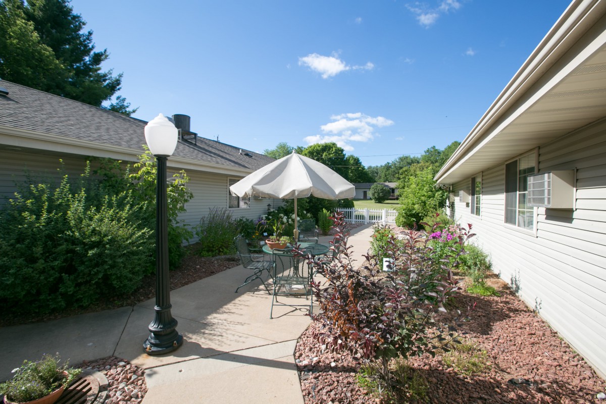 A serene outdoor patio area with a table, chairs, and an umbrella surrounded by lush landscaping.