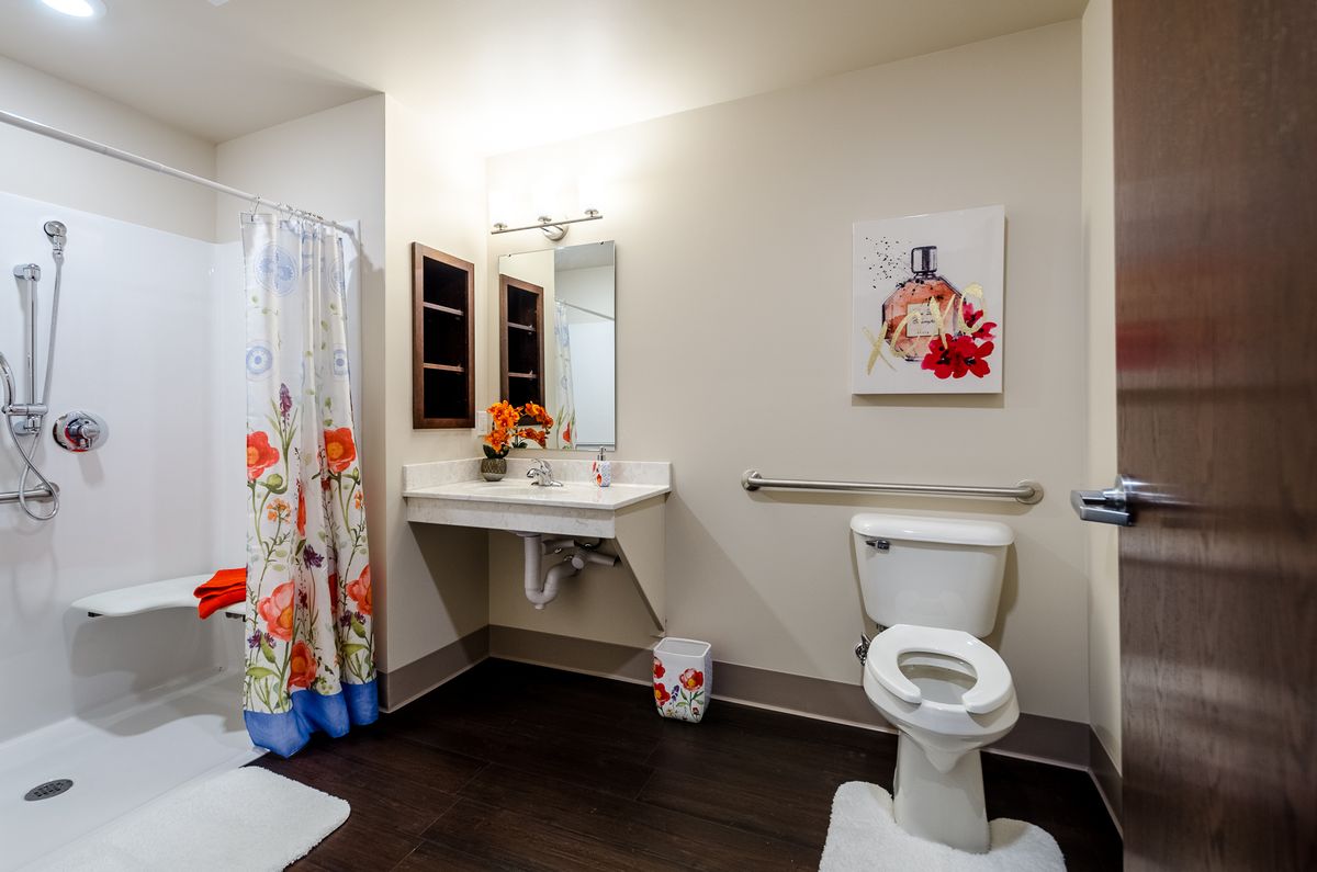 A clean and well-organized bathroom with a floral shower curtain and decorative artwork on the wall.