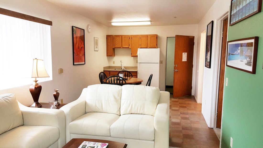 A cozy apartment living area with a white sofa, dining table, and a compact kitchen.