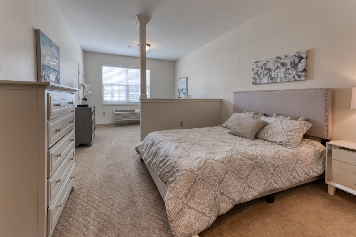 A cozy and well-lit bedroom with a bed, dresser, and large window.