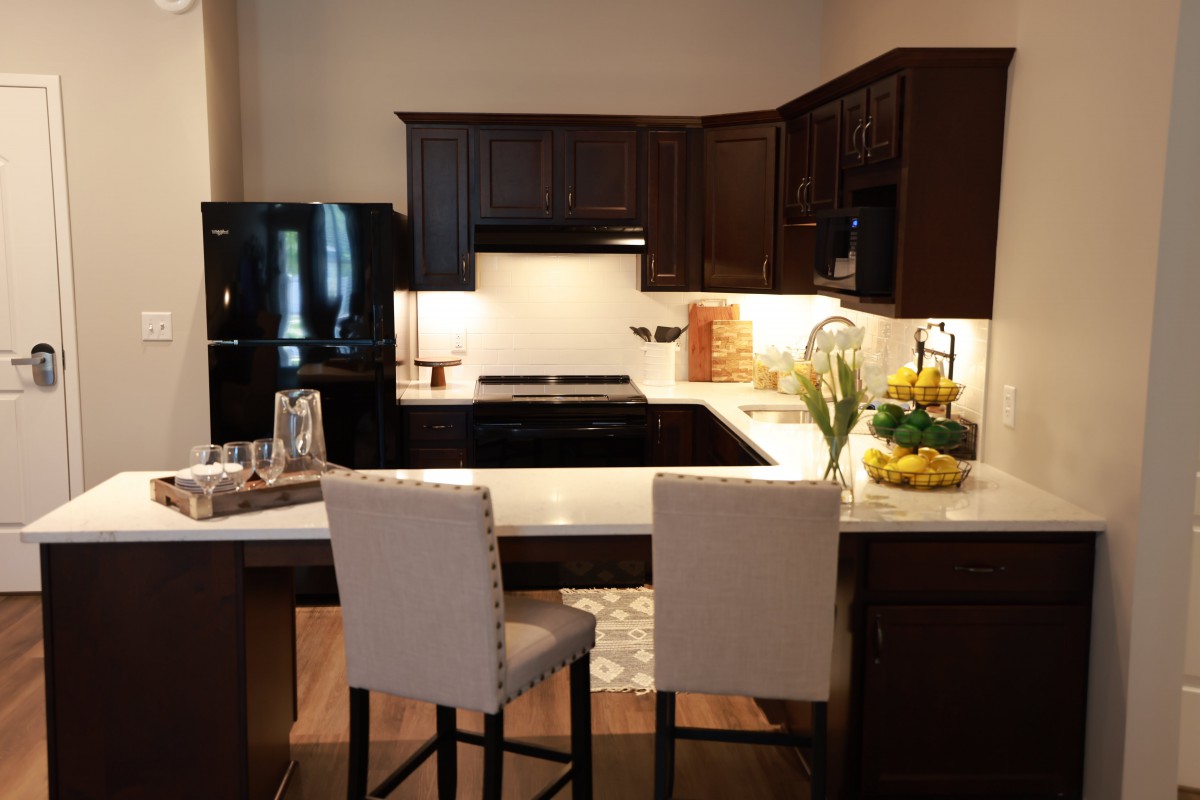 A modern kitchen with dark wood cabinets and black appliances, featuring a cozy seating area with bar stools.