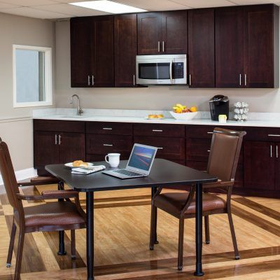A modern office kitchen setup with a table and chairs, featuring a laptop and various kitchen appliances.