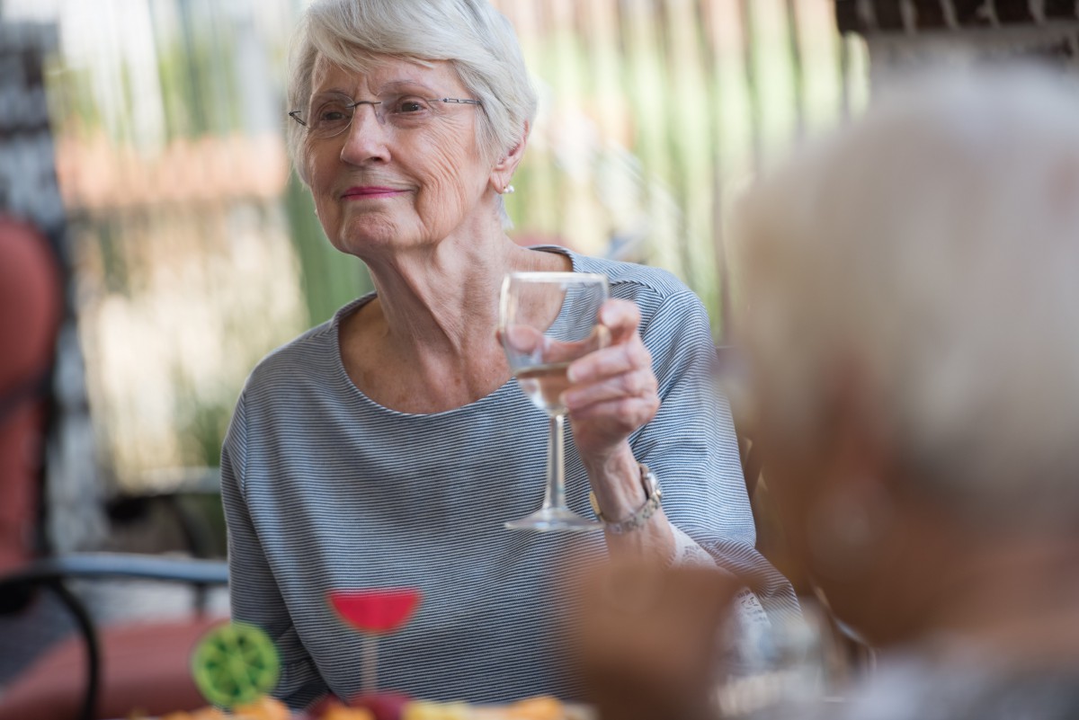 An elderly woman enjoying a drink at an outdoor social gathering.