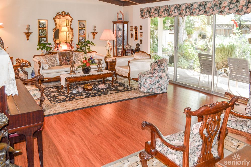A traditional living room with elegant furnishings, featuring a hardwood floor, plush rug, and large sliding glass doors that provide natural light.