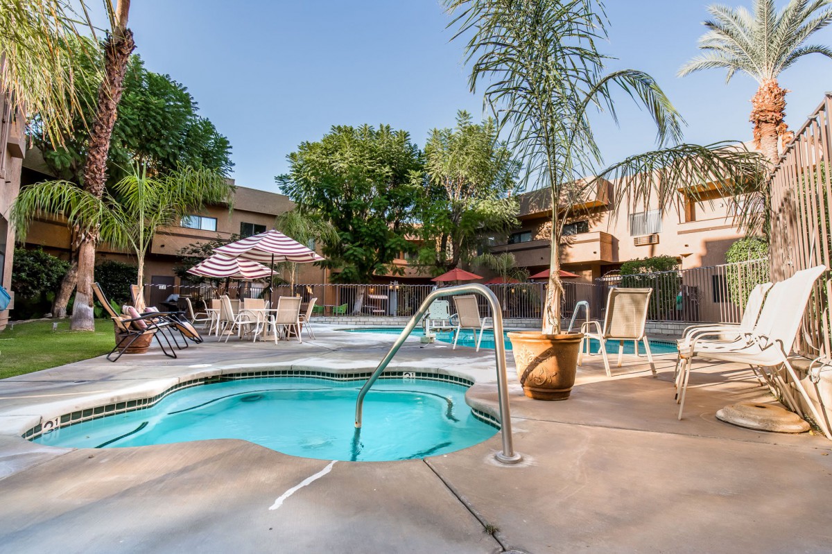 A serene outdoor resort area featuring a swimming pool and hot tub, surrounded by palm trees on a sunny day.