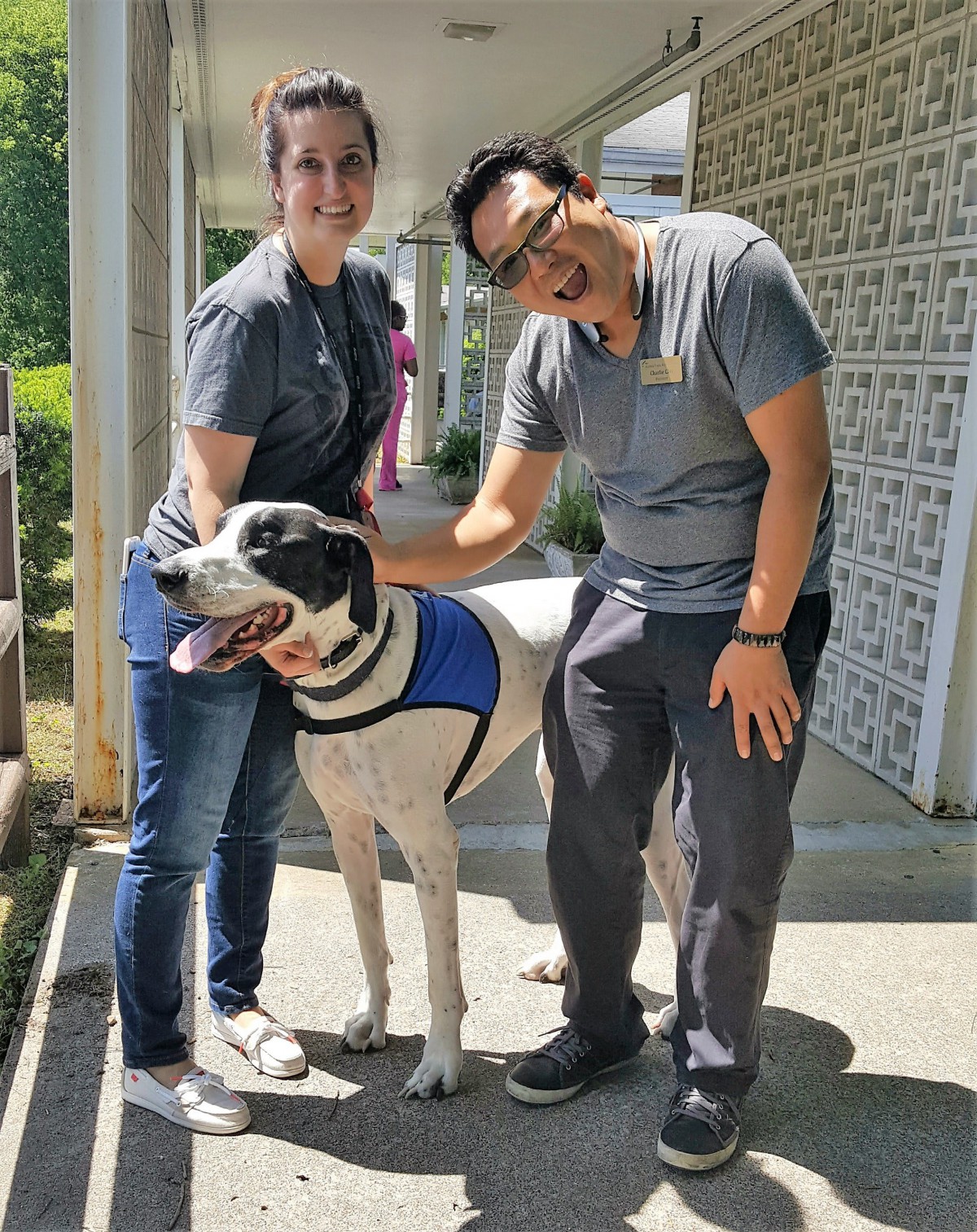 Two people happily petting a large dog outdoors.