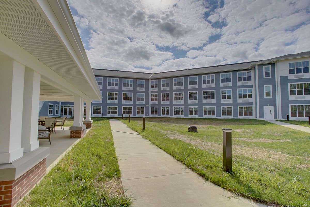 A wide-angle view of a modern multi-story building with a pathway and grass lawn under a partly cloudy sky.