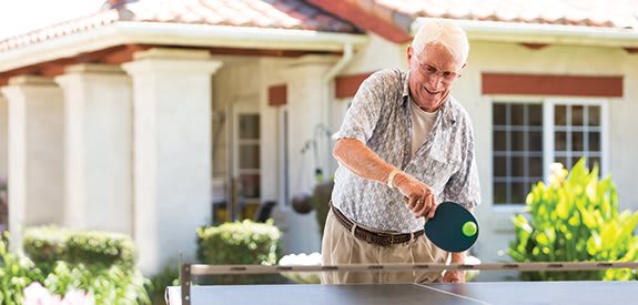 A senior man playing table tennis outdoors, enjoying a leisurely game.