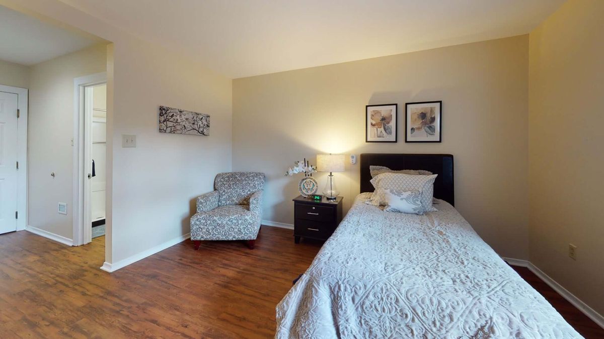 A cozy bedroom with a single bed, an armchair, and wall art.