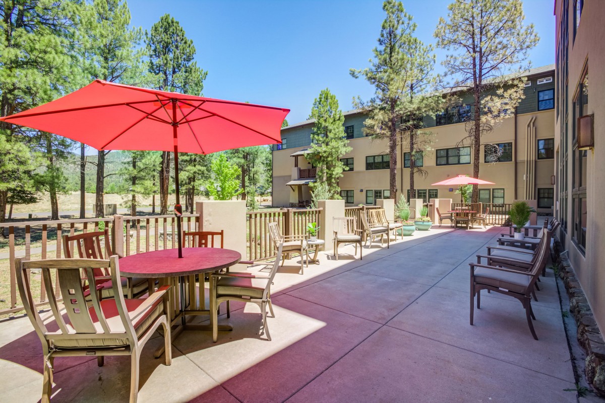 Outdoor patio area with tables and umbrellas, surrounded by trees and buildings on a sunny day.