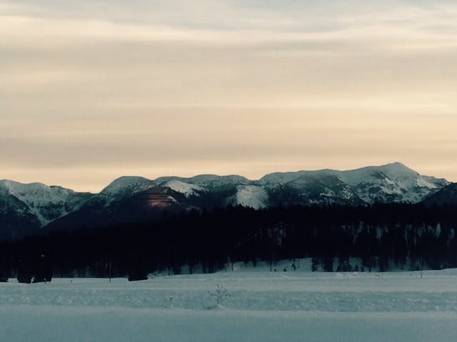 A serene winter landscape with snow-covered mountains at sunset.