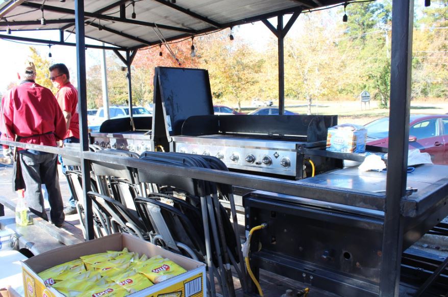 Outdoor grilling setup under a shelter with cooking equipment and autumn background.