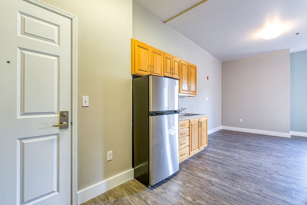 A modern apartment kitchen with wooden cabinets and a stainless steel refrigerator.