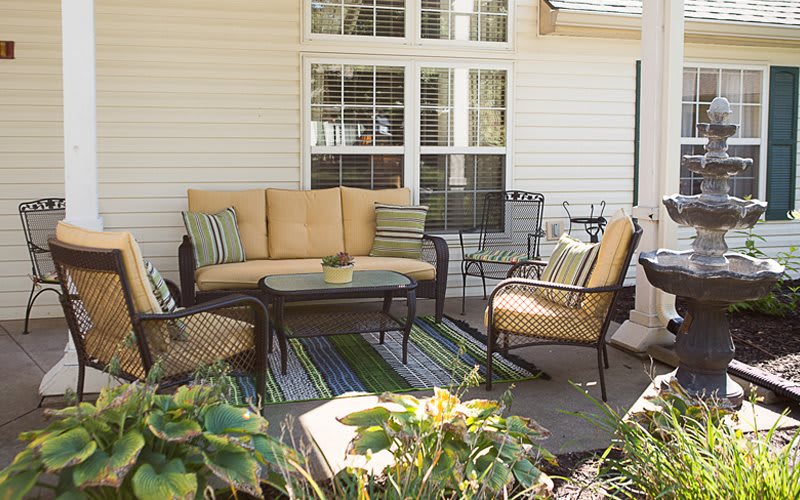 A cozy outdoor patio setup with a sofa, chairs, table, and cushions beside a house.