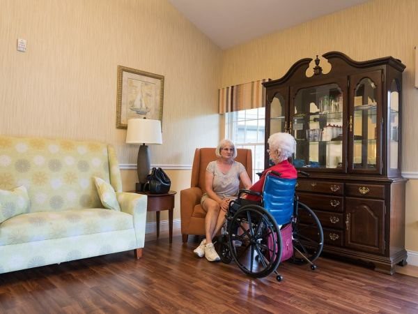 Two elderly individuals sit in a comfortable living room, engaged in conversation.
