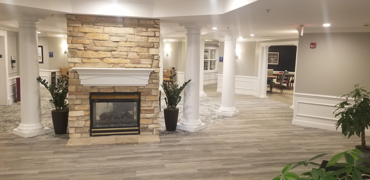 A modern living room featuring a stone fireplace, elegant white columns, and wood flooring.