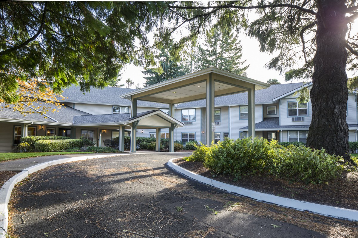 A residential building with a large driveway and surrounded by trees.