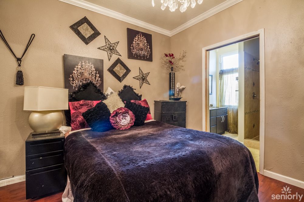 A cozy bedroom with elegant decor and a plush comforter, featuring stylish artwork and a chandelier.