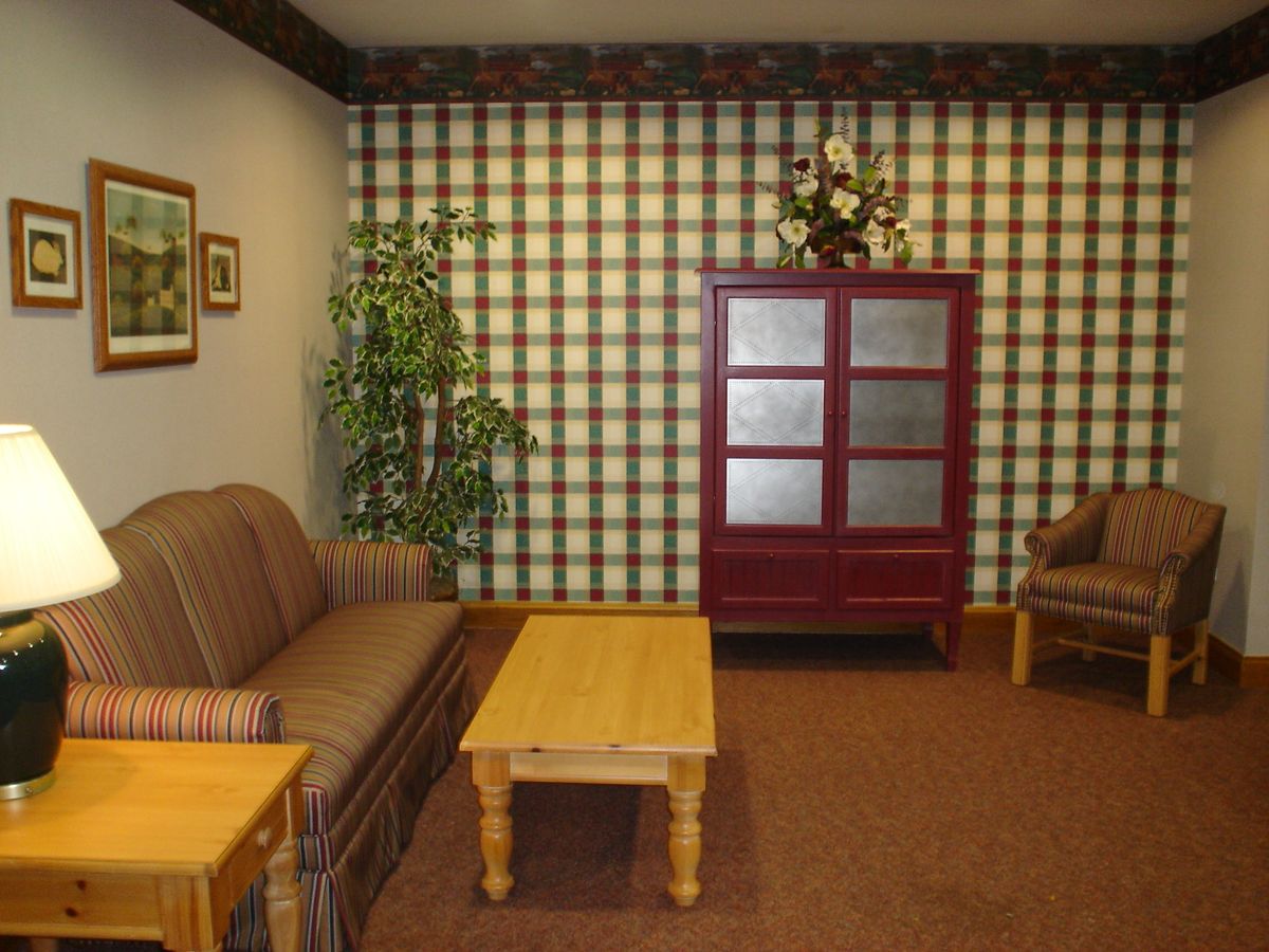 A cozy living room with plaid wallpaper, featuring a sofa, armchair, coffee table, and a red cabinet.
