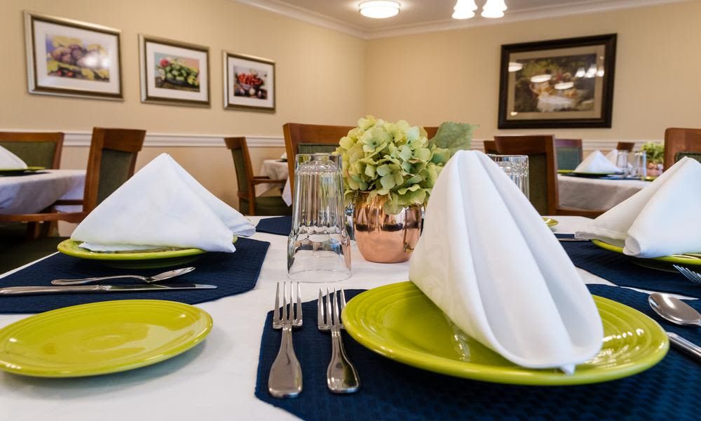 A neatly arranged dining table with green plates, white napkins, and a floral centerpiece.