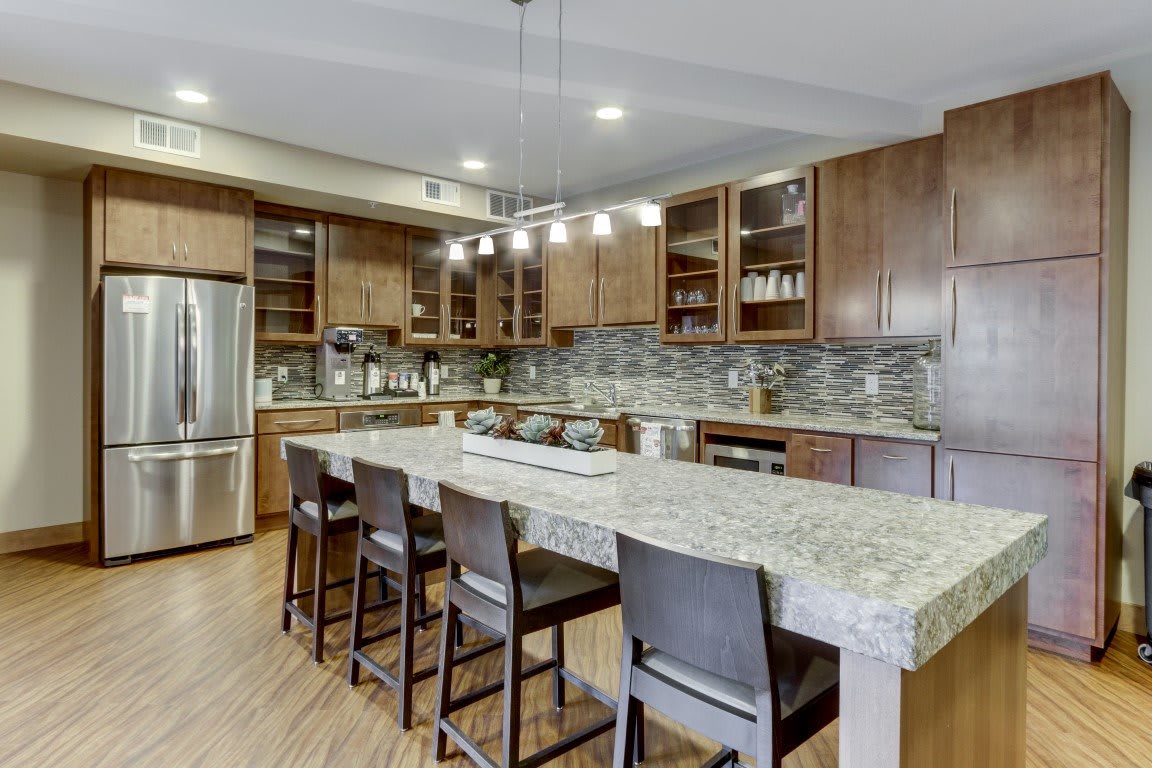 A modern kitchen featuring wood cabinets, a large granite island with bar stools, and stainless steel appliances.